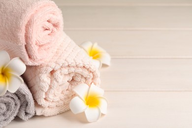 Closeup view of soft folded towels and plumeria flowers on white wooden table, space for text