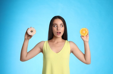 Woman choosing between orange and doughnut on light blue background