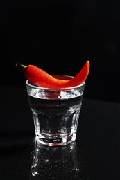 Photo of Red hot chili pepper and vodka in glass on black table