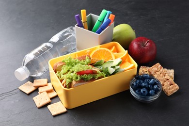 Photo of Lunch box with healthy food for schoolchild and markers on black textured table