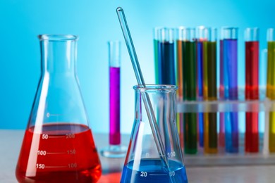 Photo of Different laboratory glassware with colorful liquids on wooden table against light blue background, closeup