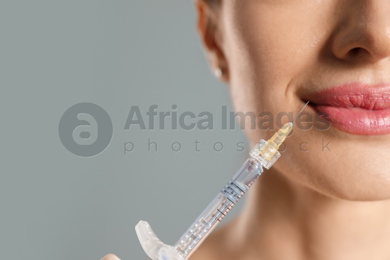Beautiful woman getting facial injection on grey background, closeup. Cosmetic surgery