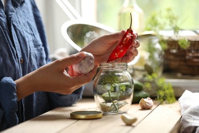 Woman putting pepper into jar in kitchen, closeup