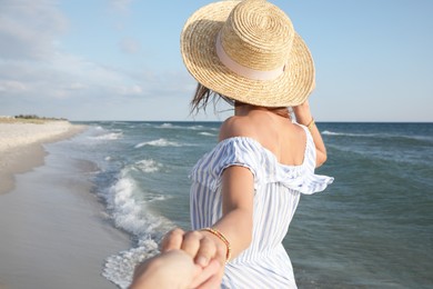 Woman with straw hat holding her lover's hand near sea on sunny day