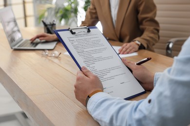 Photo of Man reading employment agreement at table in office, closeup. Signing contract