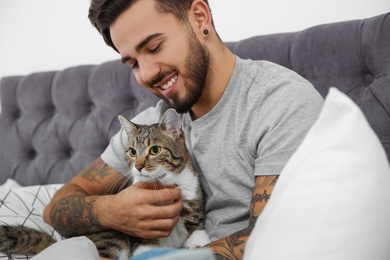 Happy man with cat on bed at home. Friendly pet