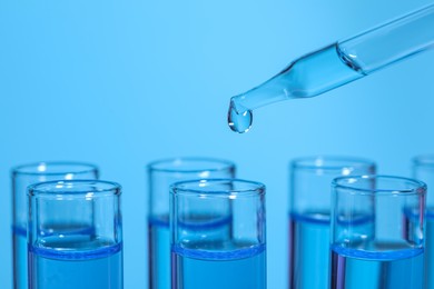 Dripping reagent into test tube on light blue background, closeup and space for text. Laboratory analysis