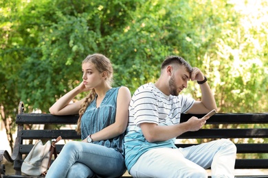 Young couple arguing while sitting on bench in park. Problems in relationship