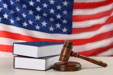 Judge's gavel and books on white wooden table against American flag
