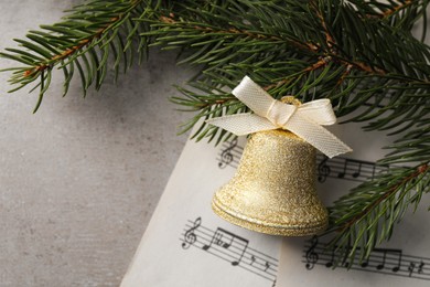 Photo of Golden shiny bell with bow, music sheets and fir branches on light table, flat lay. Space for text. Christmas decoration