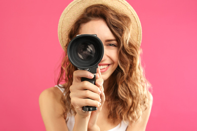 Beautiful young woman using vintage video camera against crimson background, focus on lens