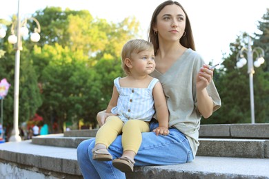 Photo of Mother with cigarette and child outdoors. Don't smoke near kids