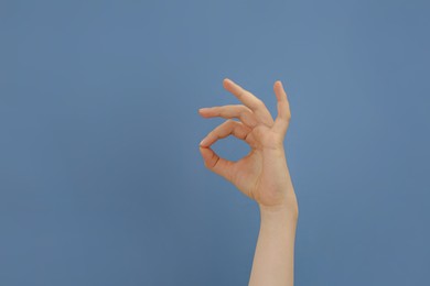 Woman showing okay gesture on pale blue background, closeup