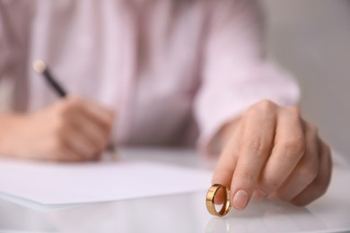 Woman with wedding ring signing divorce papers at table indoors, closeup. Space for text