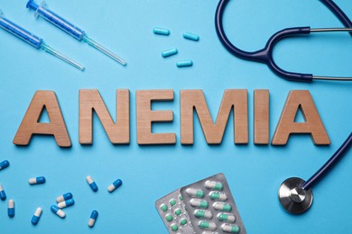 Photo of Word Anemia, pills, syringes and stethoscope on light blue background, flat lay