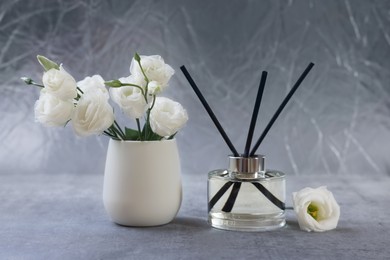 Photo of Reed diffuser and vase with eustoma flowers on gray marble table
