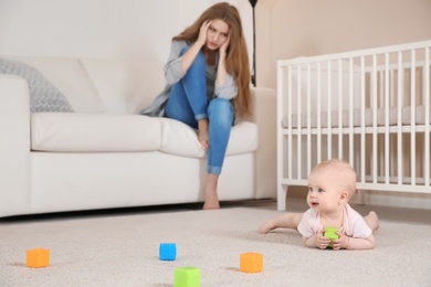 Photo of Cute baby girl playing on floor and young mother suffering from postnatal depression at home