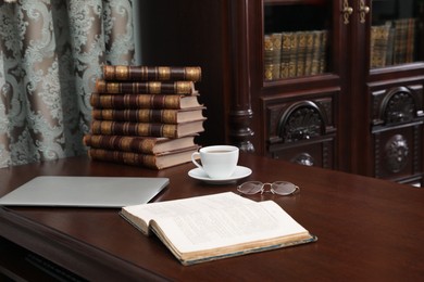 Photo of Laptop, books and cup of coffee on wooden table in library reading room