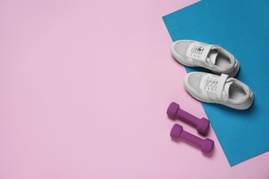Exercise mat, dumbbells and shoes on pink background, flat lay. Space for text