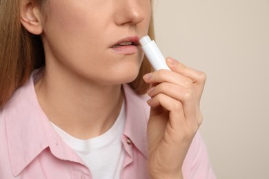 Woman with herpes applying lip balm against beige background, closeup