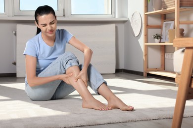 Young woman rubbing sore leg at home. Space for text