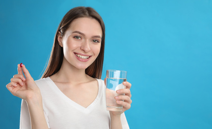 Young woman with vitamin pill and glass of water on blue background
