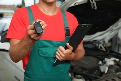 Photo of Mechanic with clipboard and car key at automobile repair shop, closeup