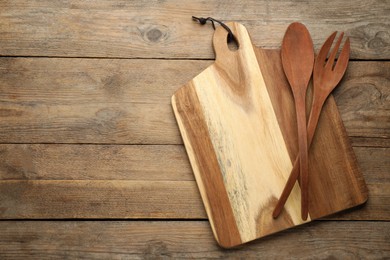 Cutting board, spoon and fork on wooden table, top view with space for text. Cooking utensils