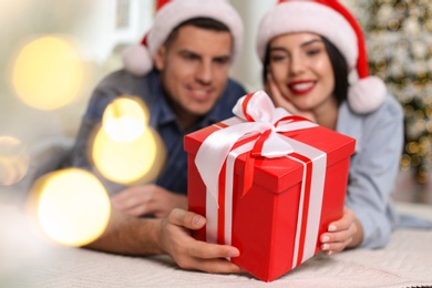Happy couple with Christmas gift box at home, focus on hands