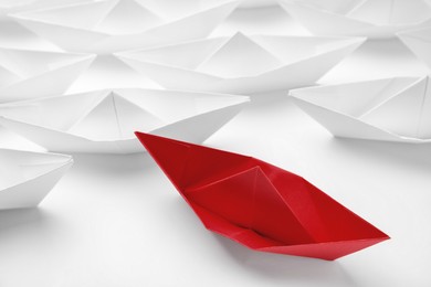 Photo of Red paper boat floating away from others on white background, closeup. Uniqueness concept