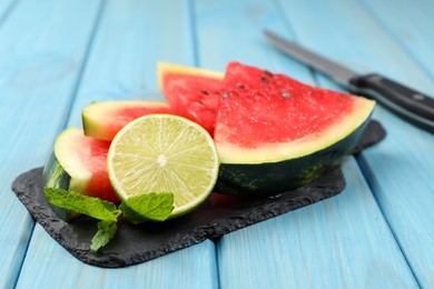 Slate board with cut watermelon and lime on light blue wooden table