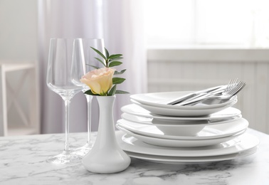 Set of clean dishes and vase with flower on white marble table