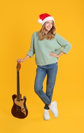 Young woman in Santa hat with electric guitar on yellow background. Christmas music