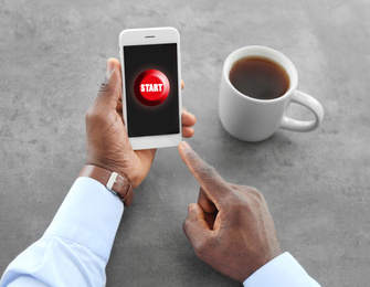 African-American man pointing at start icon on smartphone at table, closeup