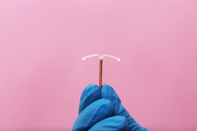 Doctor holding T-shaped intrauterine birth control device on pink background, closeup