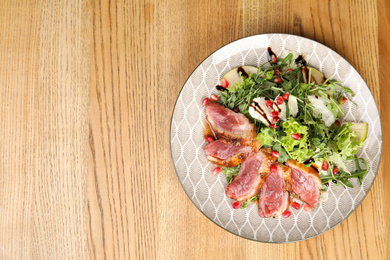 Photo of Delicious salad with roasted duck breast served on wooden table, top view. Space for text