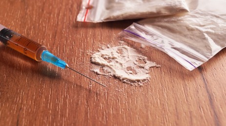 Photo of Plastic bags of powder and syringe on wooden table, closeup. Hard drugs