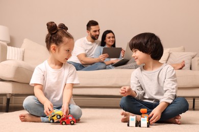 Cute children playing with toys while parents using gadgets on sofa in living room