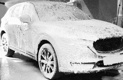 Worker cleaning automobile with high pressure water jet at car wash