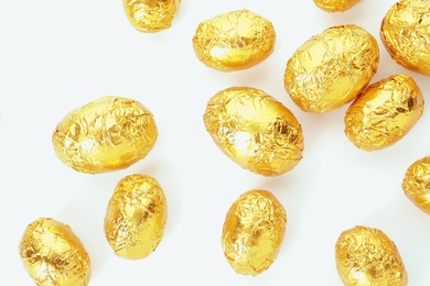 Many chocolate eggs wrapped in bright golden foil on white background, top view