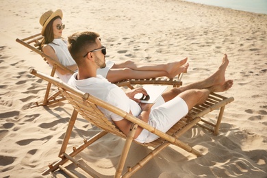 Young couple relaxing in deck chairs on sandy beach