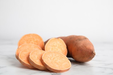 Whole and cut ripe sweet potatoes on white marble table