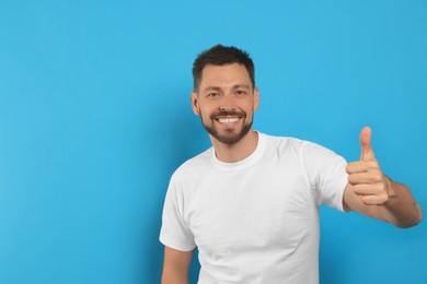 Man showing thumb up on light blue background, space for text