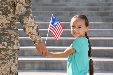 Soldier and his little daughter with American flag holding hands outdoors. Veterans Day in USA