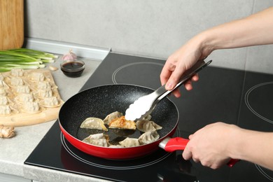 Woman cooking gyoza on frying pan with hot oil in kitchen, closeup
