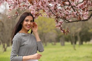 Photo of Pretty young woman near blooming tree in park, space for text. Spring look