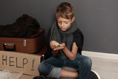 Poor homeless boy begging on floor near dark wall