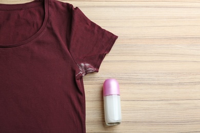 T-shirt with stain and deodorant on wooden background, top view. Space for text
