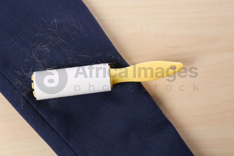Photo of Lint roller and sleeve of jacket covered with hair on wooden table, flat lay