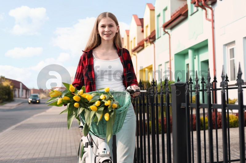 Beautiful teenage girl with bicycle and bouquet of yellow tulips on city street